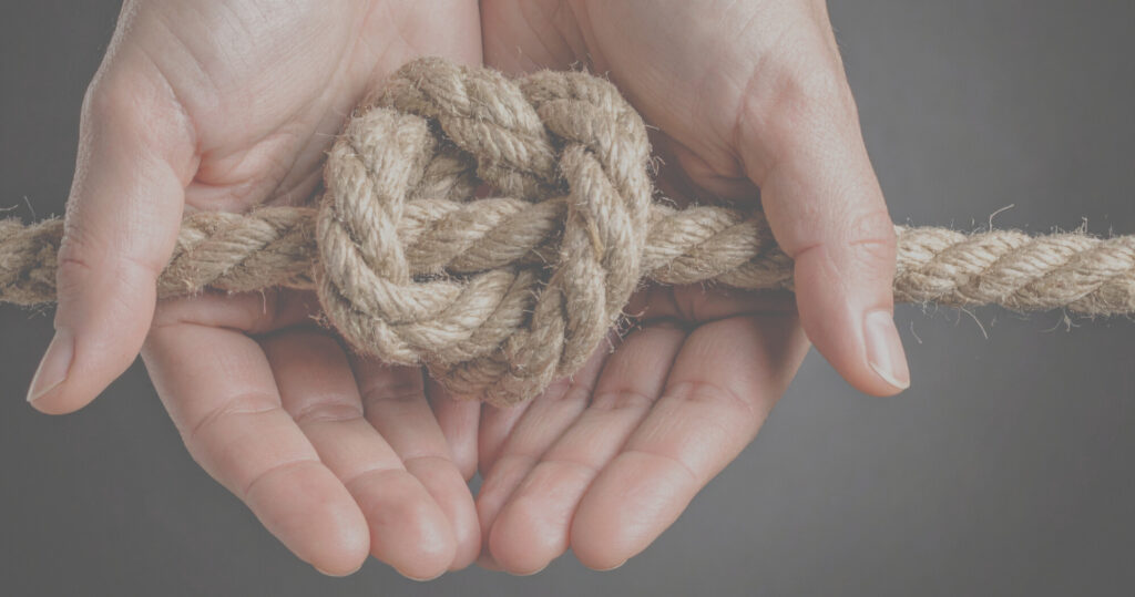 Zwei Hände halten sanft ein dickes Seil mit einem großen, zentralen Knoten vor einem unifarbenen Hintergrund, der Gleichgewicht und Verbundenheit symbolisiert - Schlüsselprinzipien der Osteopathie.
